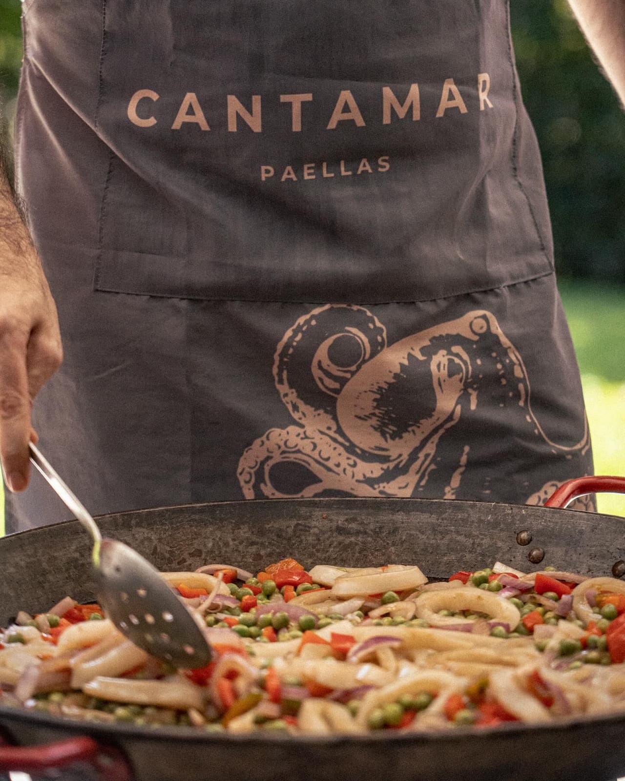 Delantal de Cantamar con un pulpo bordado, junto a la paellera